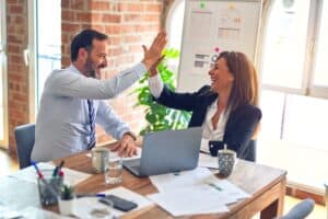professional man and woman sitting at conference table working and high fiving each other