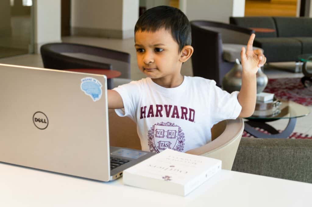 boy with harvard shirt looking at computer raising hand asking thoughtful questions