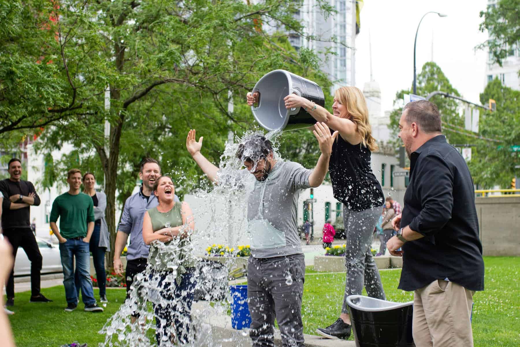 group in park woman pouring cold water on man's head in sales challenge