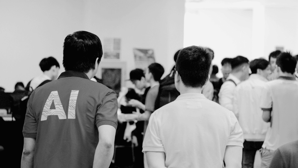 black and white photo of a group of people at a tech convention. One guy has AI printed on his shirt. Written by chatgpt