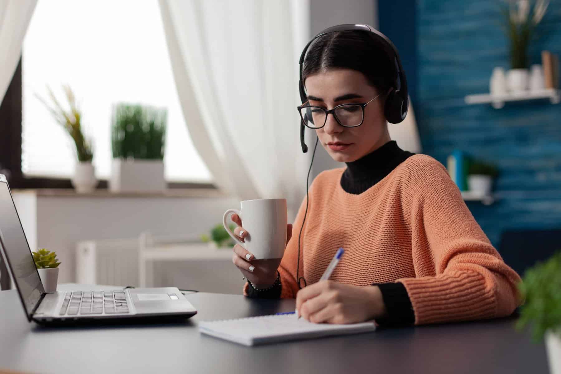 woman at desk holding coffee cup and writing in journal