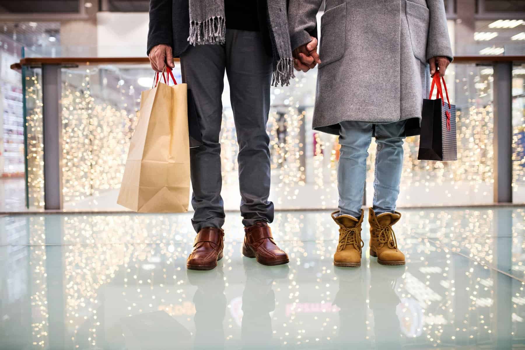 two people shown from waist down in heavy coats holding shopping bags at the mall