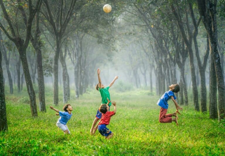 4 boys playing with a ball in field surrounded by trees