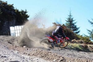 off rode motorcycle and rider taking a sharp right turn spraying up sand.