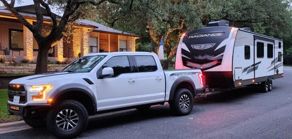 ford raptor truck and radiance travel trailer parked in front of house