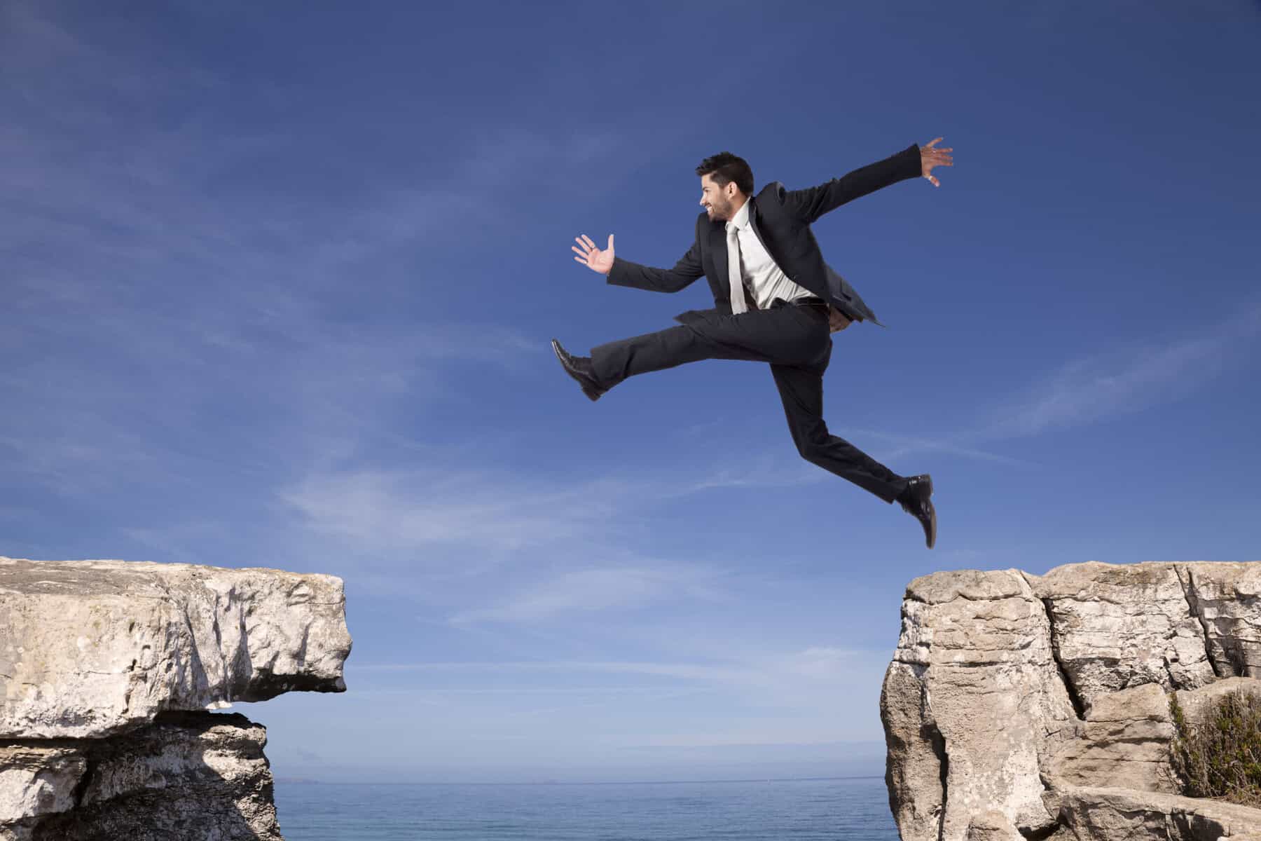man in suit leaping from one gray boulder to another signifying the courage of a buyer facilitator