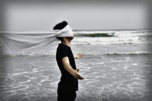 man in black standing at the ocean with arms widespread and blindfolded
