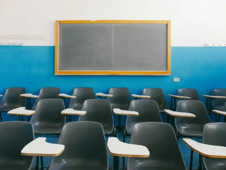 Articles 4 Empty classroom full of black chairs with side desks with a clean chalkboard against a blue and white wall in the background