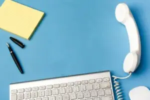 image with light blue background, note pad, open pen, keyboard, white telephone receiver