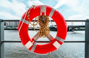 bright orange lifesaver ring and rope hanging on rail with water in background