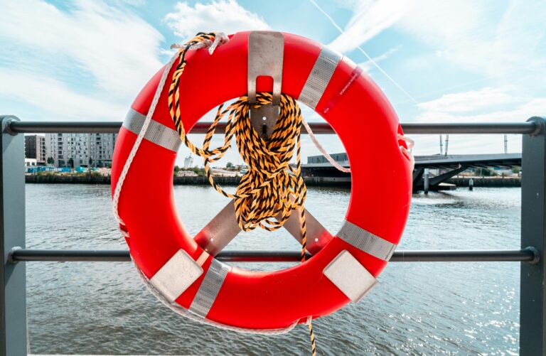 Articles 2 bright orange lifesaver ring and rope hanging on rail with water in background