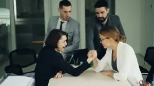 two women arm wrestling while two men look on and cheer