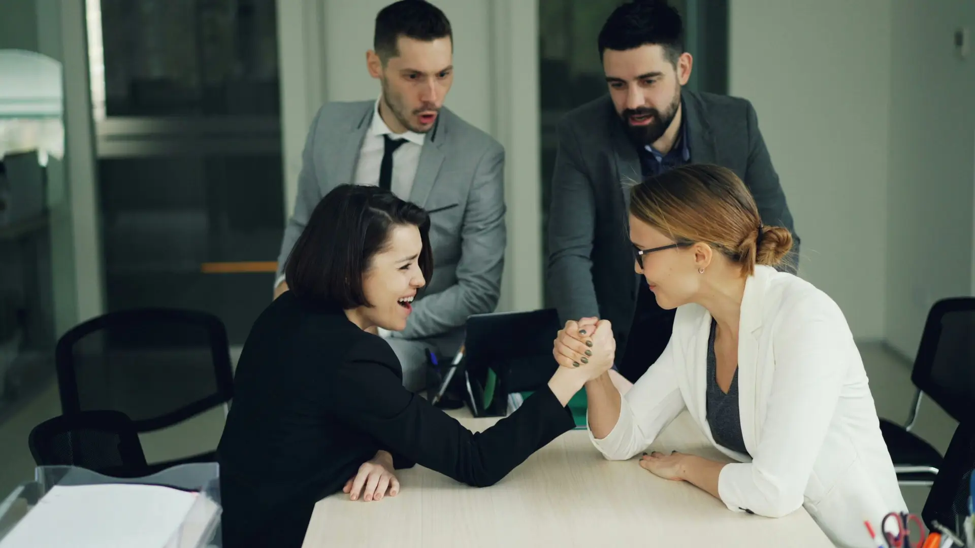 two women arm wrestling while two men look on and cheer